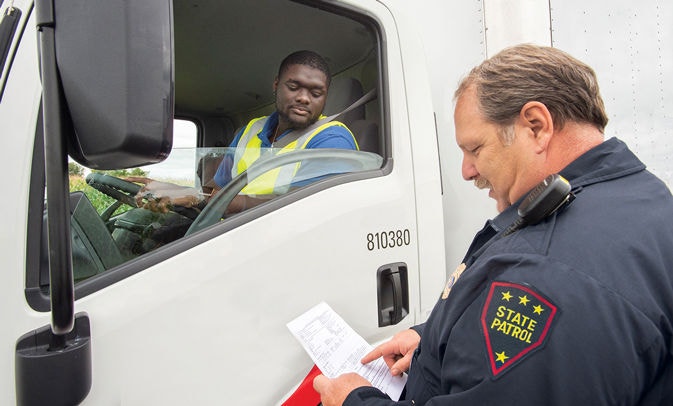 Officer looking at truck driver's documents by truck