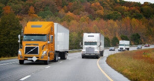 Semi trucks driving on highway with fall foliage