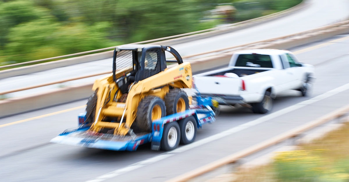 white pickup truck pulling a trailer with skidsteer