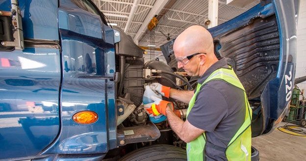 Worker in high visibility safety vest adding fluid to a large truck engine area